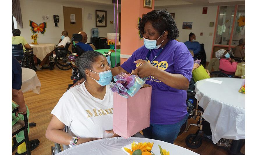 Extended Care Adopt-a-Resident Day 5-15-2025 Staffer in purple handing woman gift for web